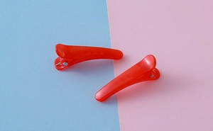 Paire de pinces à cheveux crocodile rouge translucide sur fond pastel rose et bleu