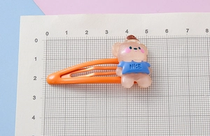 Detail showing an orange metal BB clip with a translucent resin bear and NICE text