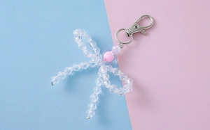 Detalle del colgante de lazo con cuentas de cristal y toque rosa sobre fondo azul y rosa