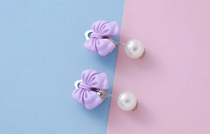 Detail of cute purple bow ear clips with resin pearls for children without piercings