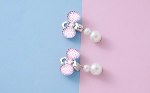 Close-up of pink resin bow clip-on earrings with elegant hanging white pearls