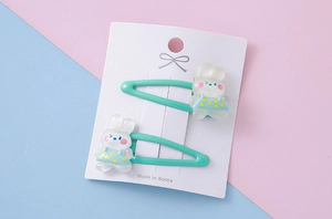Close-up of cute white resin bunnies on green drop-shaped metal hair clips for kids