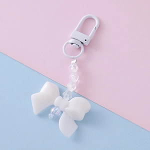 Detailed view of white acrylic bow keychain with transparent beads on pink and blue backdrop
