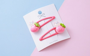 Detail of pink strawberry and rabbit hair clips for kids on a paper display card