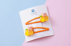 Close-up of kids hair clips with cute lemon and bear resin charms on orange metal BB clips