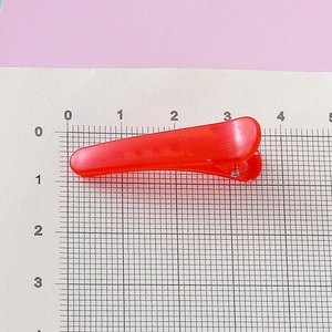 Pince à cheveux bec de canard en résine rouge translucide de 3,5 cm sur papier quadrillé