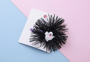 Detail of Halloween hair clip with black pom-pom and white ghost motif on purple metal base
