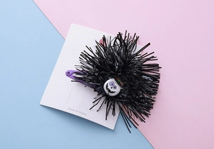 Detail of Halloween hair clip featuring black tinsel pom and cute skull with a purple metal clip