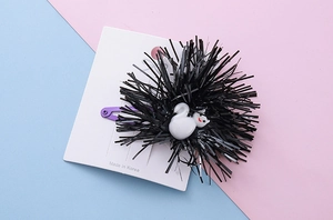 Detail of purple hair clip with black tinsel pom and white cartoon kitten charm