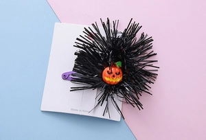 Detail of Halloween hair clip with black pompom and orange pumpkin on a purple clip