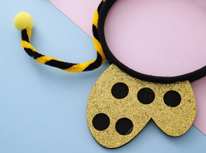 Dettaglio dell'antenna a pompon giallo e ala glitterata dorata su fascia per capelli
