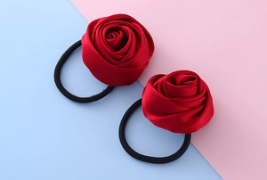 Dettaglio di elastici per capelli con rose in raso rosso su uno sfondo color pastello