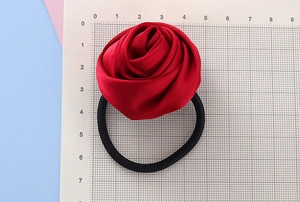 Dettaglio dell'elastico per capelli con rosa in raso rosso su griglia di misura