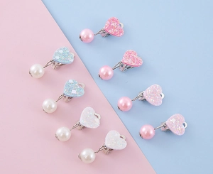 Dettaglio macro di clip per orecchie a cuore glitterato e perle per bambini colorati