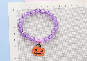 Detail of purple beaded Halloween bracelet with pumpkin charm shown on a scale ruler