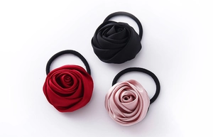 Dettaglio di tre elastici per capelli con rose in raso nero, bordeaux e rosa con elastico