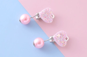 Dettaglio di orecchini a clip a forma di cuore rosa glitterato con perle finte