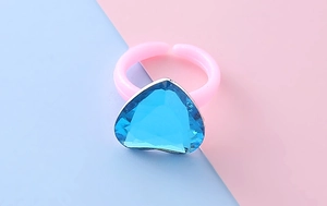 Dettaglio di una pietra preziosa blu a cuore su un anello in plastica rosa per bambine
