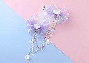 Detail of iridescent mesh bow hair clips with hanging pearl tassels and shell charms