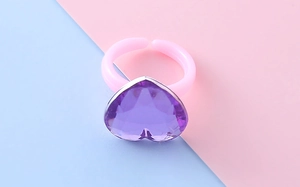 Dettaglio anello per bambini con gemma viola a cuore e fascia rosa regolabile