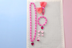 Pink cartoon jewelry set with necklace and bracelet displayed on a measuring grid board