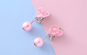Dettaglio ravvicinato di orecchini a clip con cuore rosa e perle per bambine