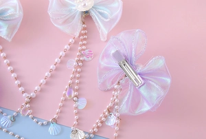 Detailed view of iridescent organza bow hair clip with faux pearl and shell tassel