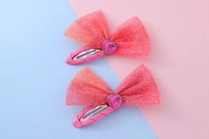 Close-up of two pink mesh heart bow hair clips with silver glitter on a pastel background