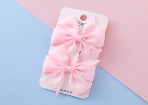 Détail de barrettes à nœuds en ruban gros-grain rose sur carte de présentation enfant