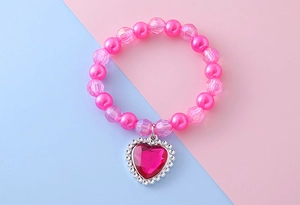 Détail d'un bracelet de perles roses pour enfant avec un grand pendentif cœur