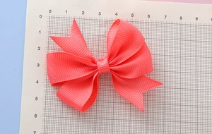 Détail d'un nœud en ruban gros-grain corail sur une règle graduée de 8cm par 5,5cm