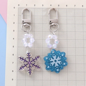 Blue and white snowflake pendant keychains with iridescent beads on a scale grid