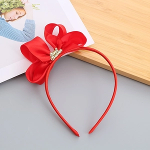 Close-up of a festive red bow headband with a golden Merry Christmas metal charm detail