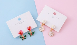 Detail of Christmas clip-on earrings with holly and snowflake designs on white card