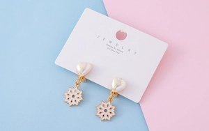 Detail view of heart and snowflake ear clips on a jewelry card with soft pastel background