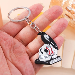 Gothic skull and black crow keychain featuring white skeleton head with a dark book