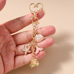 Detail of a gold ocean-themed keychain with pink starfish, seashell, and mermaid tail