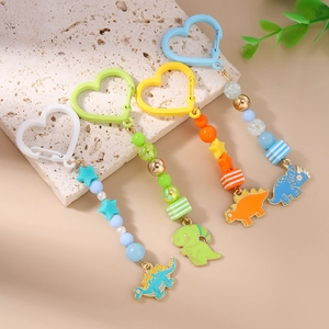Détail de porte-clés dinosaure avec fermoirs en cœur et perles colorées sur pierre