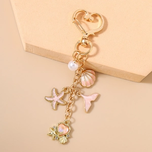 Detail of golden keychain with pearl, shell, starfish and pink heart on sandy background