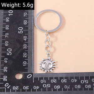 Silver metal sun keychain with 5.6g weight displayed on a ruler for size reference