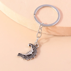 Silver crescent moon keychain with human face detail on warm pink pedestal background