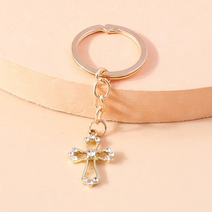 Golden hollow cross keychain with sparkling rhinestones on a minimalist beige display