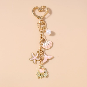 Detail of gold keychain with pink starfish, shell, fish tail charms and white pearl