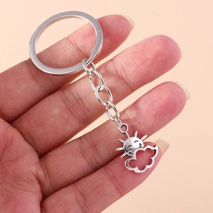 Vintage silver metal sun and cloud keychain shown held by hand on a pink background