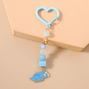 Détail d'un porte-clés dinosaure bleu avec mousqueton en cœur et perles élégantes