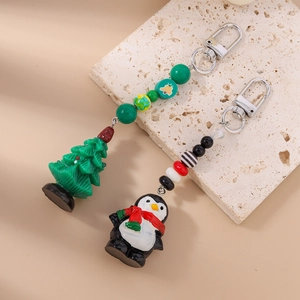 Détail du lot de porte-clés de Noël avec pingouin mignon et sapin perlé sur pierre beige