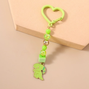 Détail d'un porte-clés dinosaure vert avec mousqueton en cœur et perles sur support beige