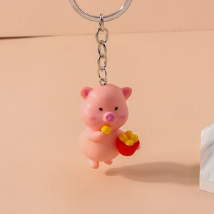 Close-up of a cute pink resin cartoon pig keychain holding fries with a gold ring