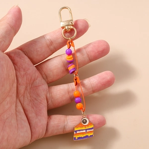 Detail of colorful beaded keychain with orange safety pins and enamel cake charm