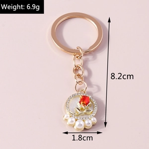 Close-up of golden rose keychain with pearls and ruby resin charms on pink background